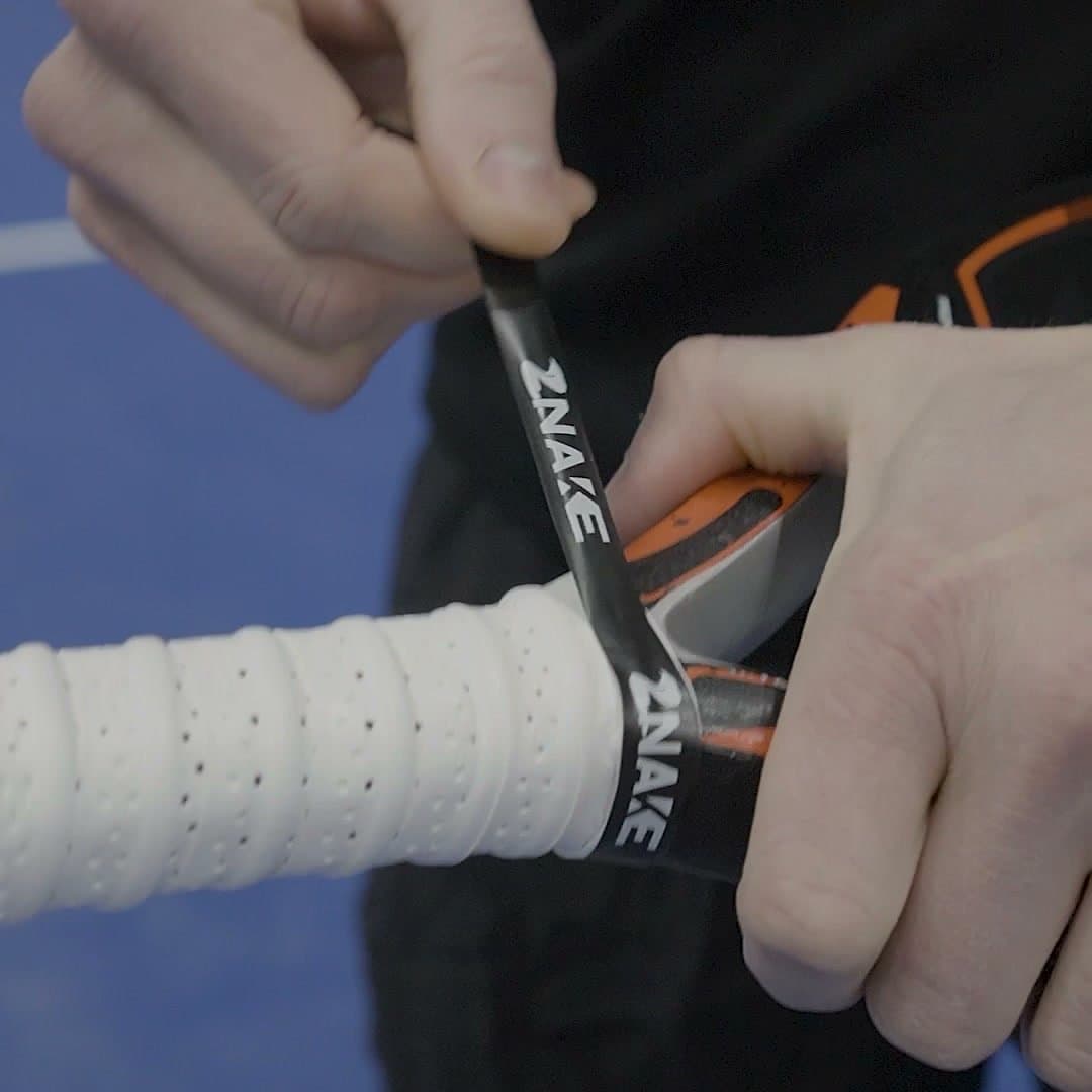 Weißer Znake Viper Overgrip wird an einem Padelschläger fertig gewickelt und mit Znake-Tape fixiert.